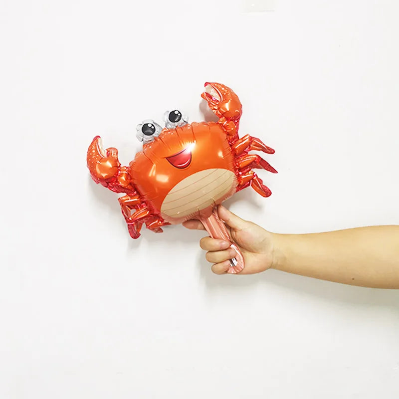 An orange foil balloon shaped like a crab is being held by a hand against a white background.