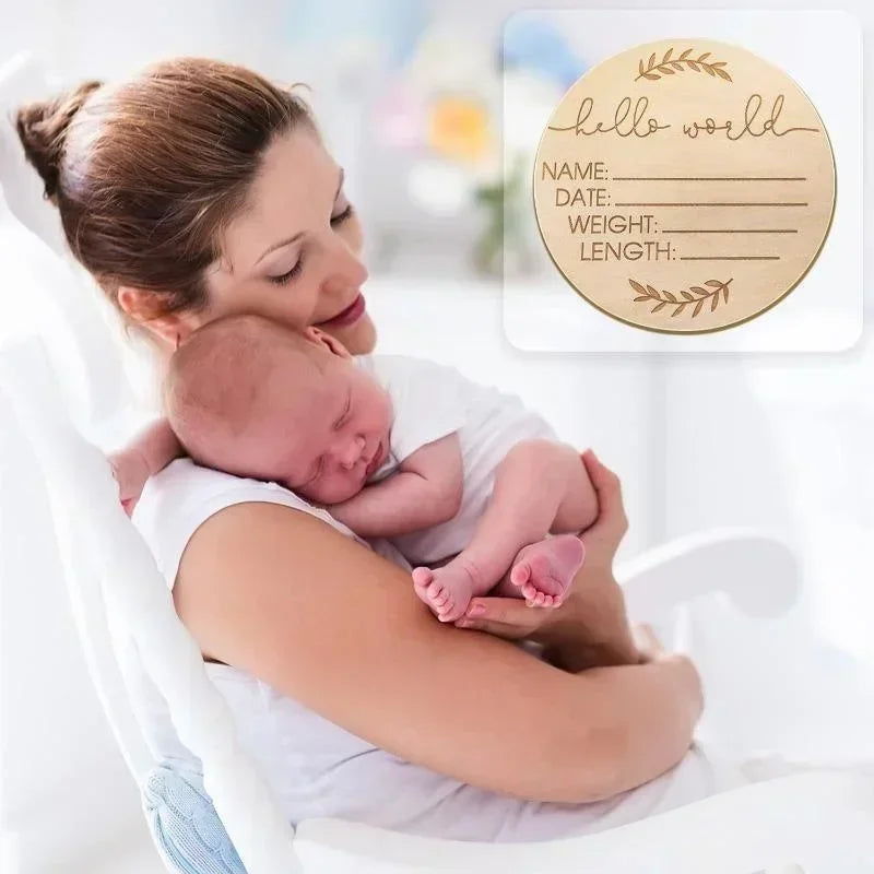 A mother holds a newborn baby while looking at a personalized wooden name announcement sign with blank lines for details.