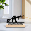 A black metal rifle statue with a wooden base engraved with custom name, displayed on a white desk.