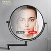 A folding double-sided wall mirror with telescopic arms showing a close-up of a woman's face and water droplets.
