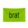 A bright lime green fabric banner with the word brat printed in black lowercase letters.