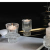 Porta-velas de cristal transparente color verde azulado con una vela encendida sobre una superficie oscura.