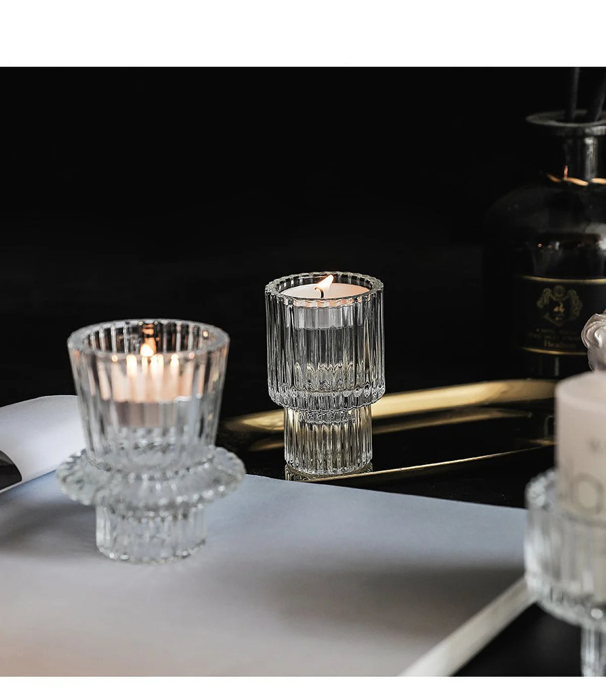 Porta-velas de cristal transparente color verde azulado con una vela encendida sobre una superficie oscura.