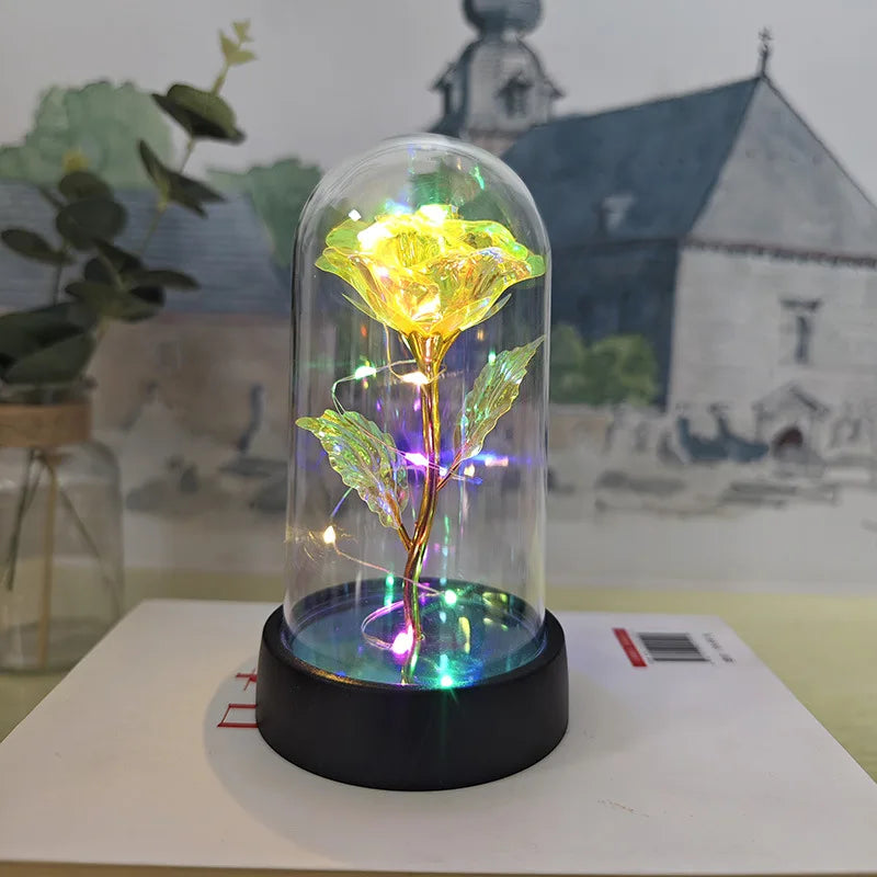 Rose de verre éternelle avec fleur jaune et feuilles vertes, illuminée par une lumière LED interne, présentée sur une surface