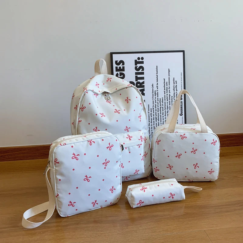 A set of white backpacks and accessories featuring a red bow print on a wooden surface.