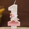 Vela de cumpleaños con forma de uno, decorada con purpurina rosa y una pequeña figura de unicornio blanco.