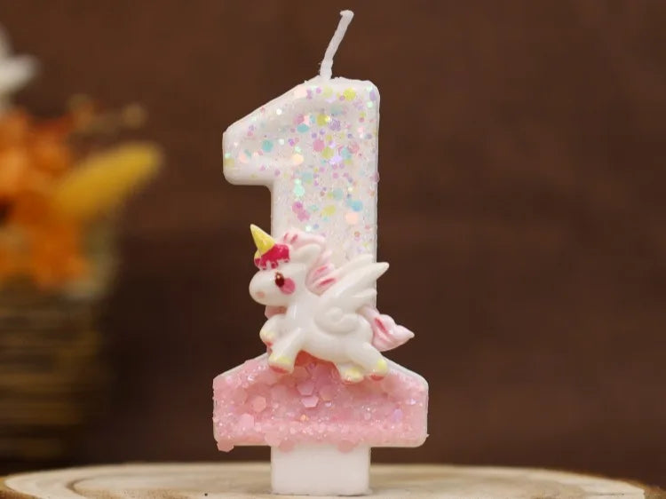 Vela de cumpleaños con forma de uno, decorada con purpurina rosa y una pequeña figura de unicornio blanco.