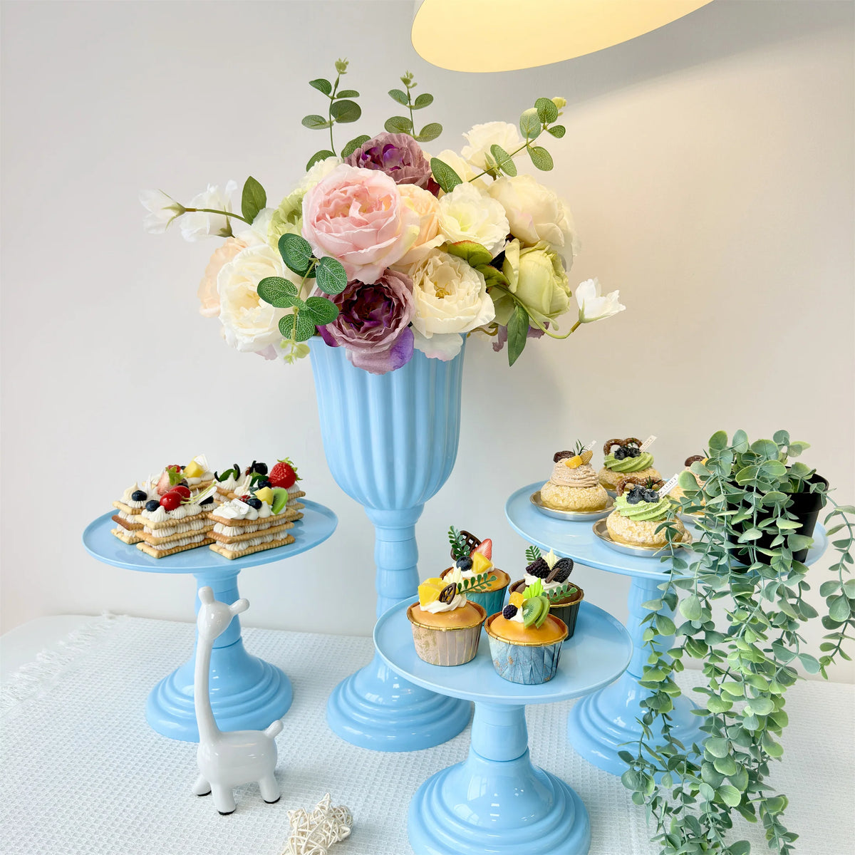A blue ceramic cylinder vase holds a bouquet of pink and cream roses and greenery on a white table.