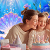A mother and two young girls posing in front of a vibrant blue underwater scene with purple and pink balloons and cake decora