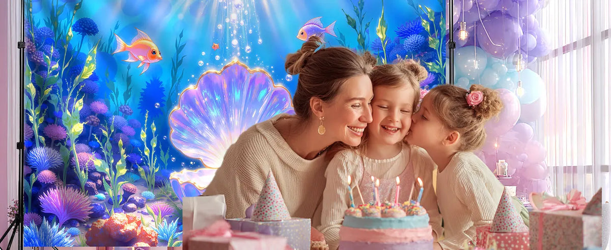 A mother and two young girls posing in front of a vibrant blue underwater scene with purple and pink balloons and cake decora