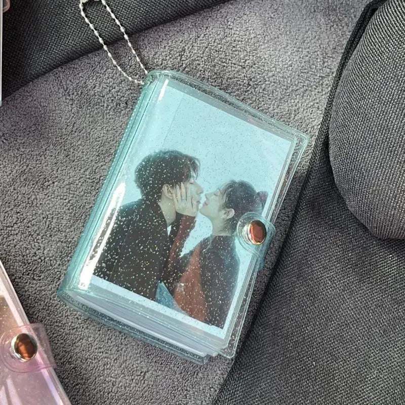A clear acrylic photo album with a silver chain attached, featuring a picture of two people kissing.