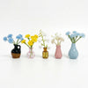A collection of mini ceramic vases holding various colorful flowers like blue and yellow blossoms.