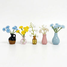 A collection of mini ceramic vases holding various colorful flowers like blue and yellow blossoms.