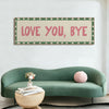 A framed canvas art print featuring the text Love You Bye in pink on a green and white checkered background above a teal sofa