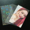 A stack of holographic card sleeves featuring a close-up photo of a woman with pink hair and glowing heart shapes.