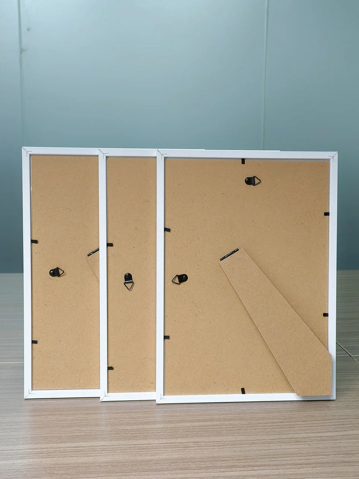 Three white picture frames with wooden fronts and acrylic borders displayed on a wooden surface.
