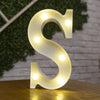A glowing warm white LED alphabet letter light shaped like the letter S resting on a wooden surface.