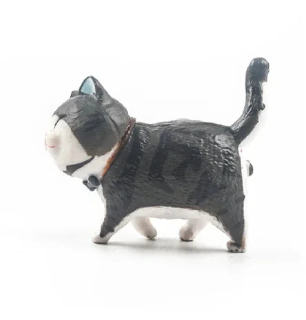 A small, dark gray and white cartoon cat figurine with a blue eye and a brown collar.