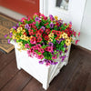 A white planter filled with a vibrant mix of artificial daisy flower bundles in shades of pink, yellow, and purple.