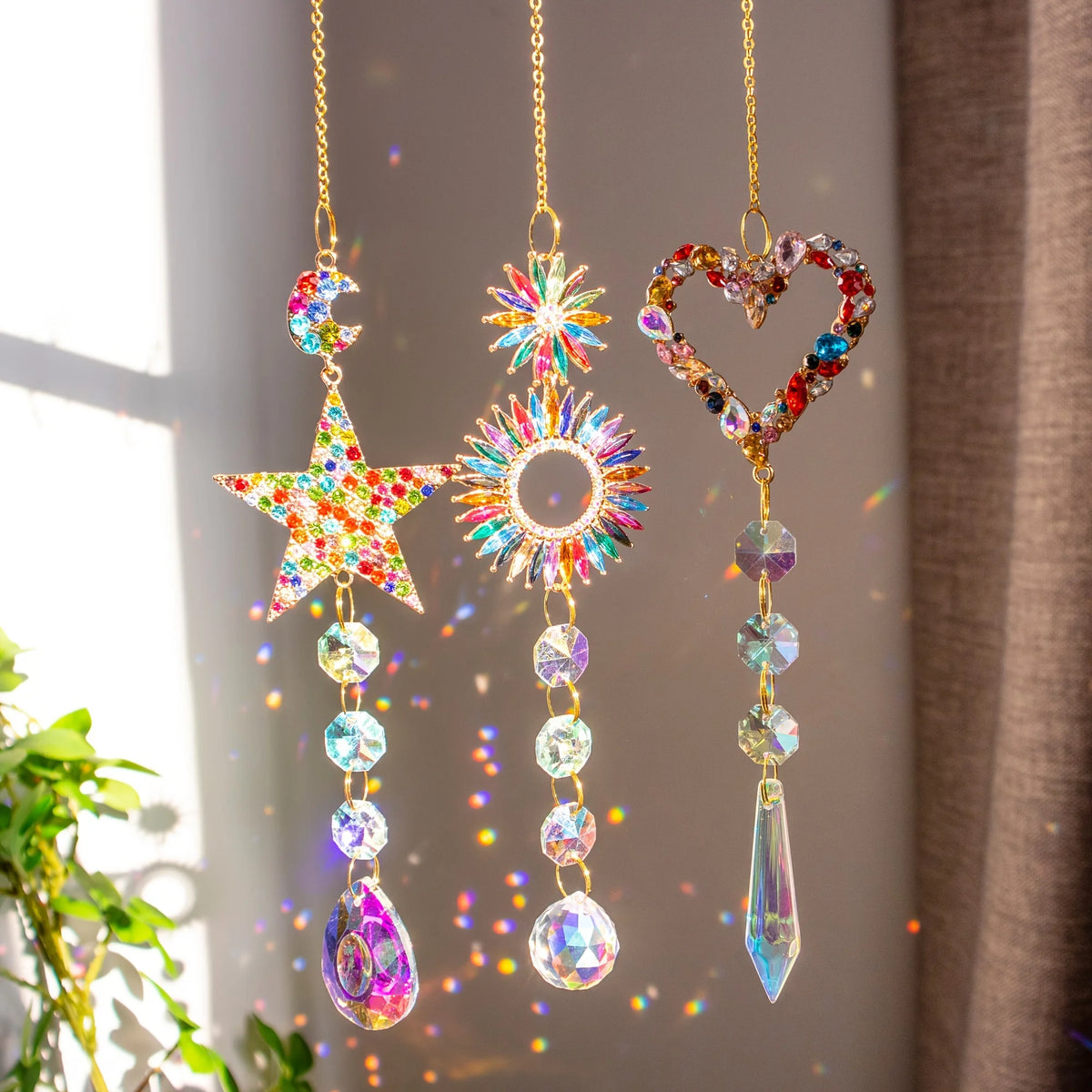 A hanging crystal rainbow sun catcher with a star, a sunburst, and a heart design.