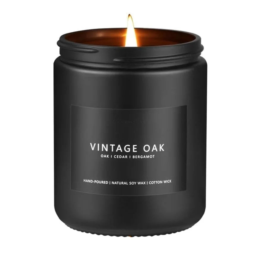 A black jar candle with a lit wick, labeled Vintage Oak scent.