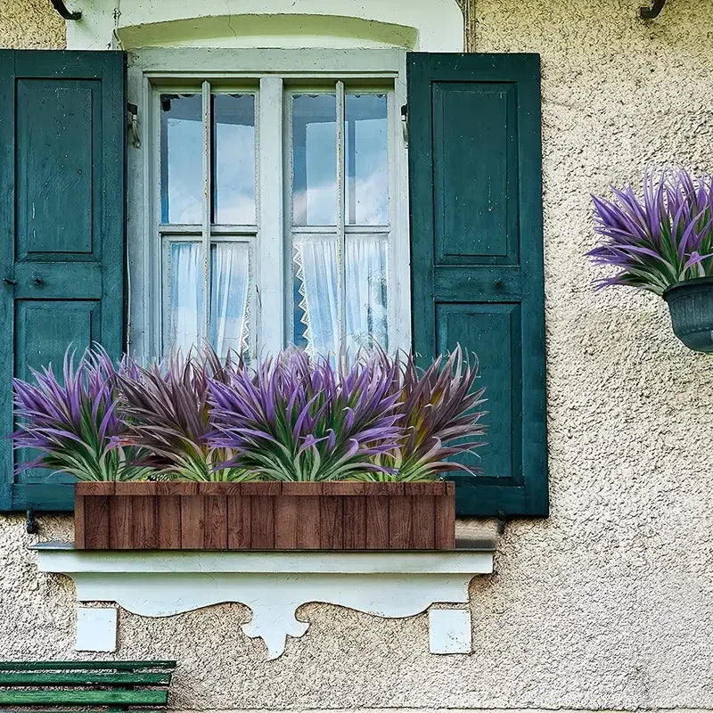 Purple artificial tall grass and tropical flowers in a wooden planter mounted on an exterior wall.