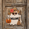 A wooden ghost door hanging featuring a witch hat design with an orange pumpkin and a welcome message