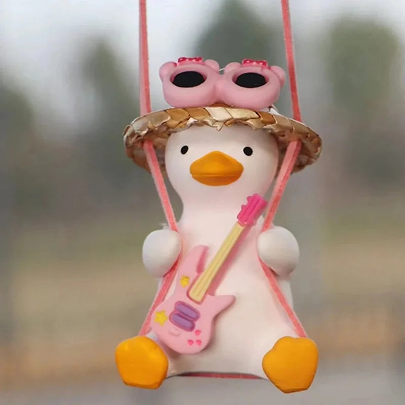 A cute pink anime duck ornament wearing pink goggles and holding a pink electric guitar, suspended by a pink string.