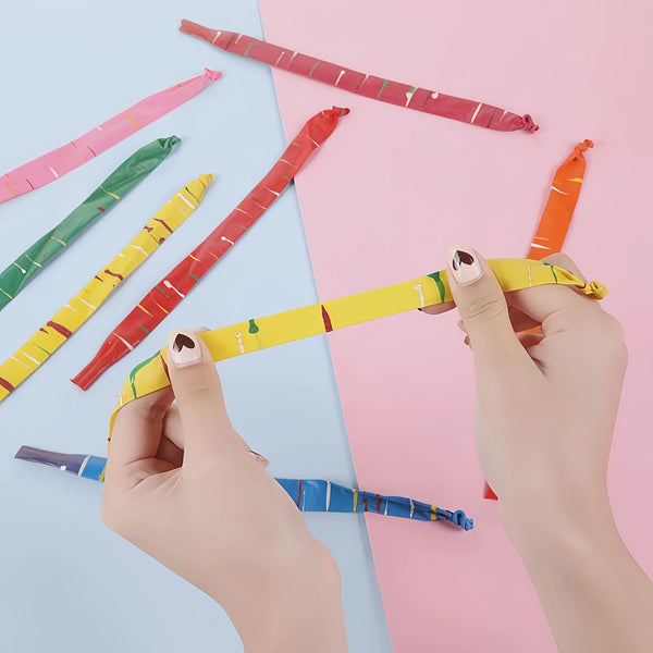 Hands holding and arranging colorful rocket balloon strips on a pink background.