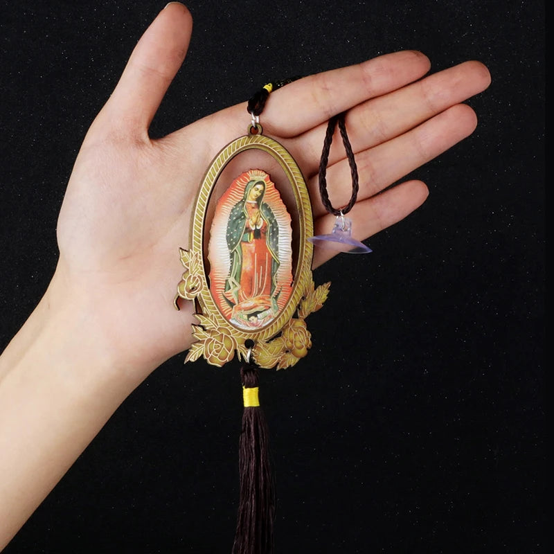 A hand holds a wooden Our Lady of Guadalupe pendant charm with a dark cord and a purple charm.
