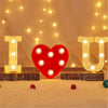 Red heart shaped luminous LED alphabet night light with glowing letters I U and a heart on a white surface
