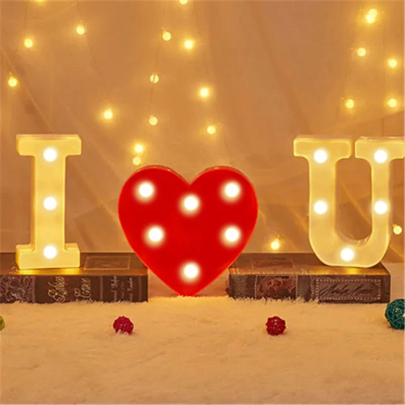 Red heart shaped luminous LED alphabet night light with glowing letters I U and a heart on a white surface