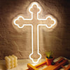 A glowing white neon cross wall sign mounted on a textured stone wall next to some wooden objects and a succulent plant.