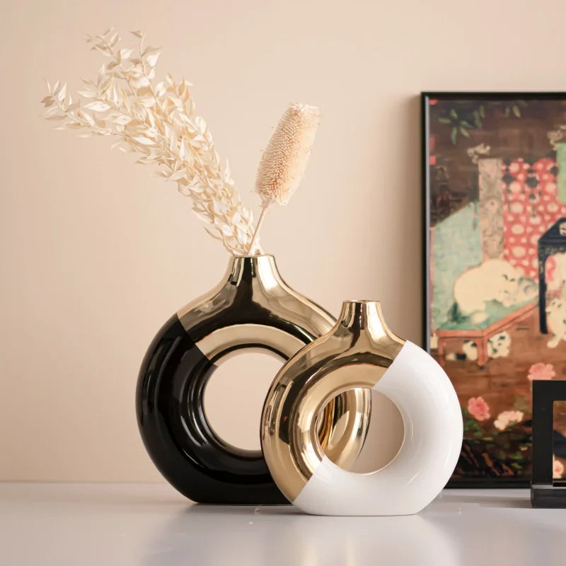 A pair of luxury ceramic flower vases, black and gold, with dried floral stems on a light surface.