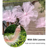 A set of three large pink sheer fabric flowers with silk leaves displayed on a wooden walkway.