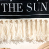 A black wall tapestry featuring the text THE SUN and a fringe border, with shadows cast below.