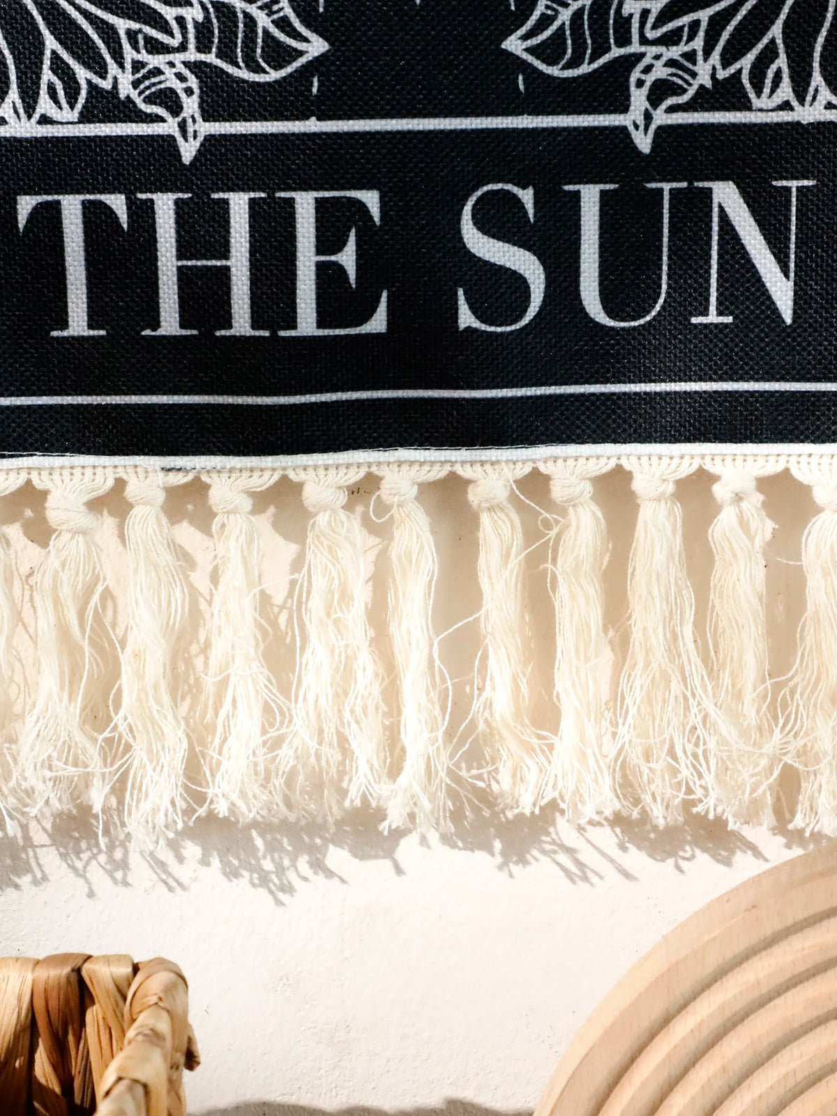 A black wall tapestry featuring the text THE SUN and a fringe border, with shadows cast below.