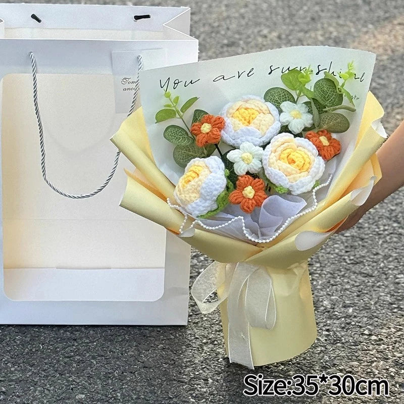 A bouquet of handmade crochet flowers in yellow and white tones is presented in a light yellow paper wrapping.