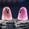 Two translucent pink ghost figurines resting on a rough gray surface against a dark blue background.