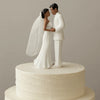A white cake topper featuring an elegant bride and groom figurine embracing.