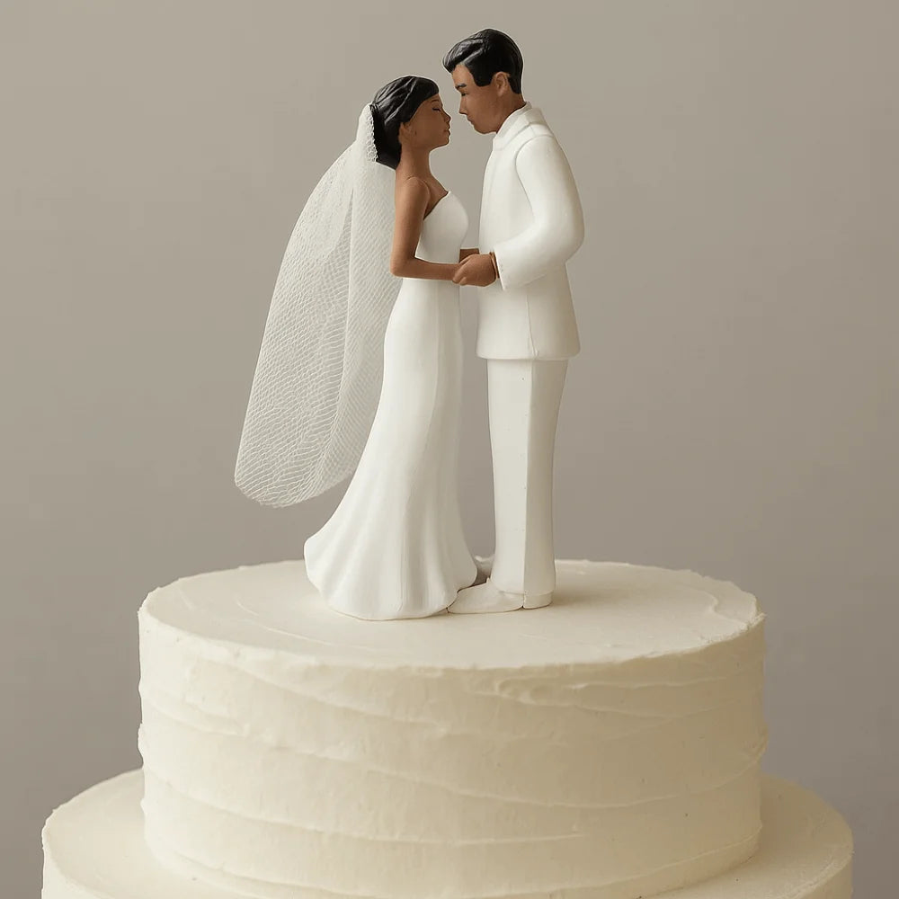 A white cake topper featuring an elegant bride and groom figurine embracing.