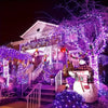 A house decorated with purple LED string lights and a large illuminated tree at night.