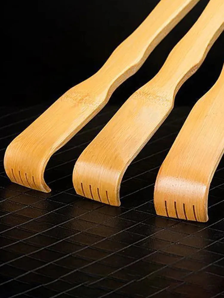 Three light wood bamboo back scratchers or roller massagers laid diagonally on a dark surface.
