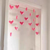 A display of pink heart-shaped string curtains hanging vertically against a white door.