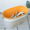 A modern boho metal hanging planter with an orange top and a light gray body sits on a black wire grid.