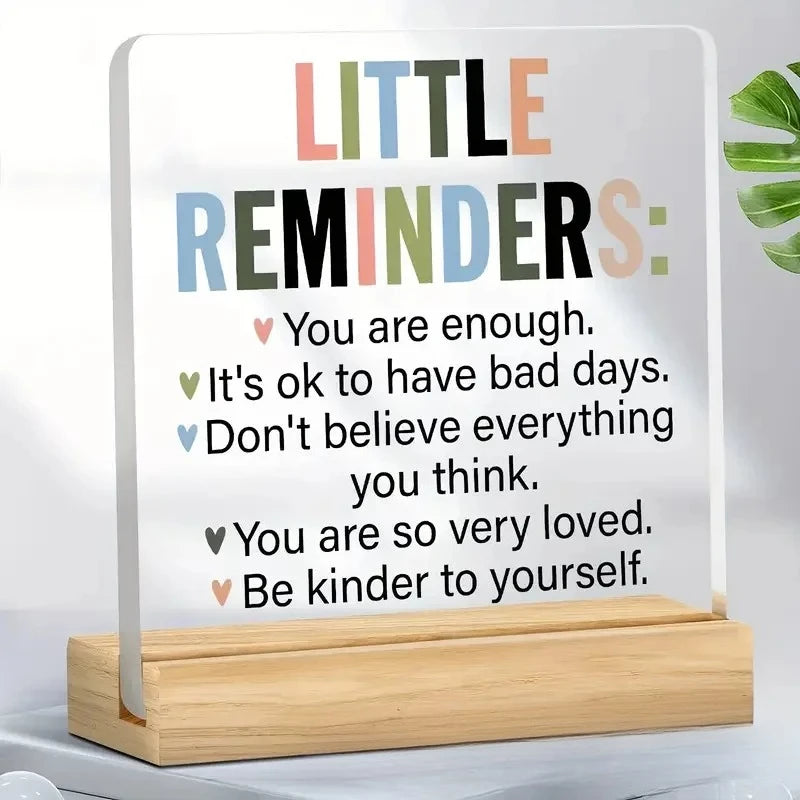 An acrylic desk sign featuring positive reminders like You are enough and Be kinder to yourself.