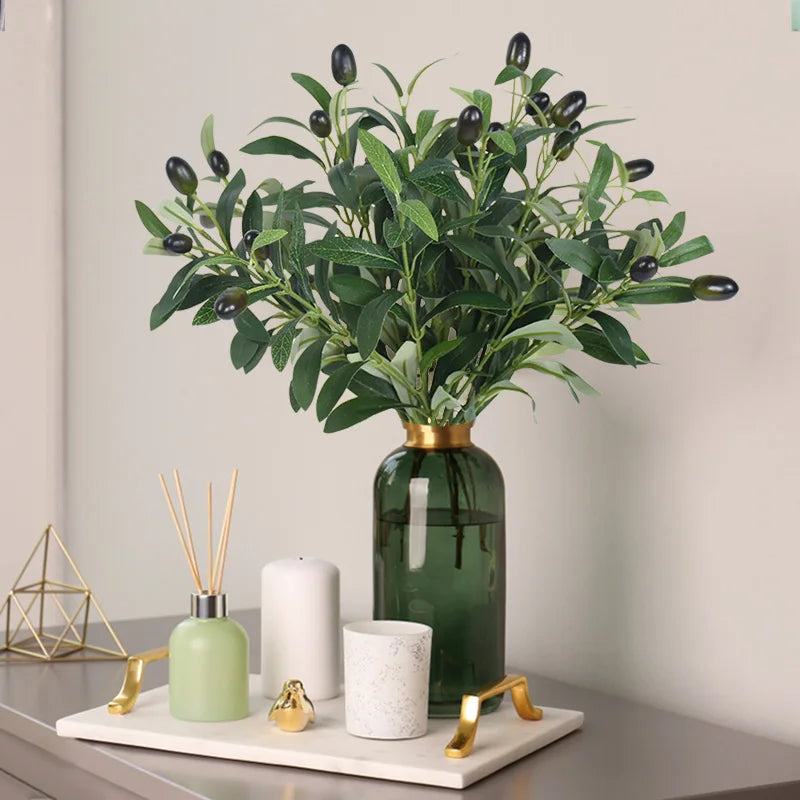 A vase filled with artificial olive leaf branches on a light gray table.