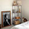 A canvas print featuring a black and white portrait of Frank Ocean's head and hand, displayed next to a metal shelving unit.