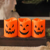 Three orange flameless LED candles shaped like carved pumpkins sitting on a dark wooden surface.