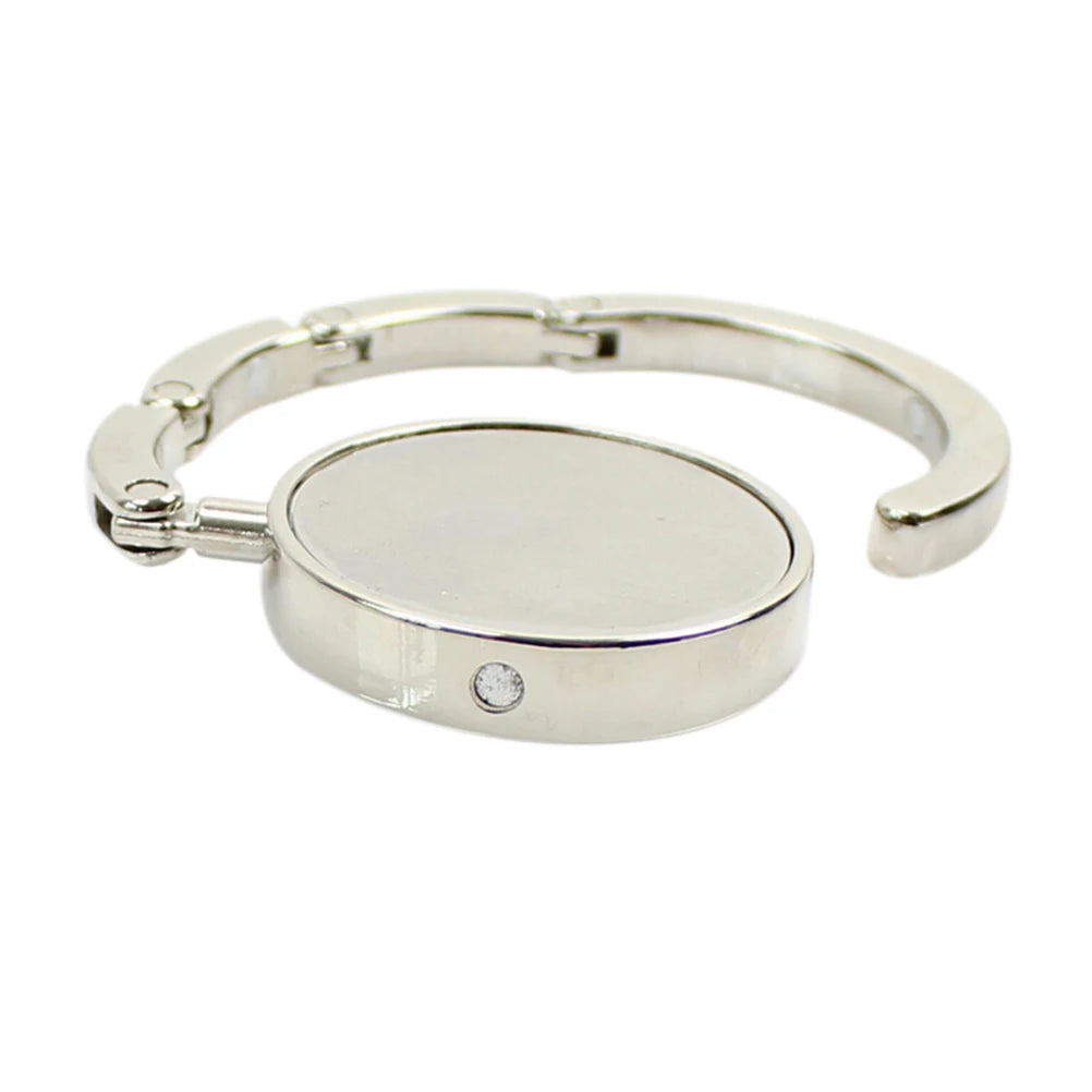 Silver foldable handbag hook designed for use on tables and desks.